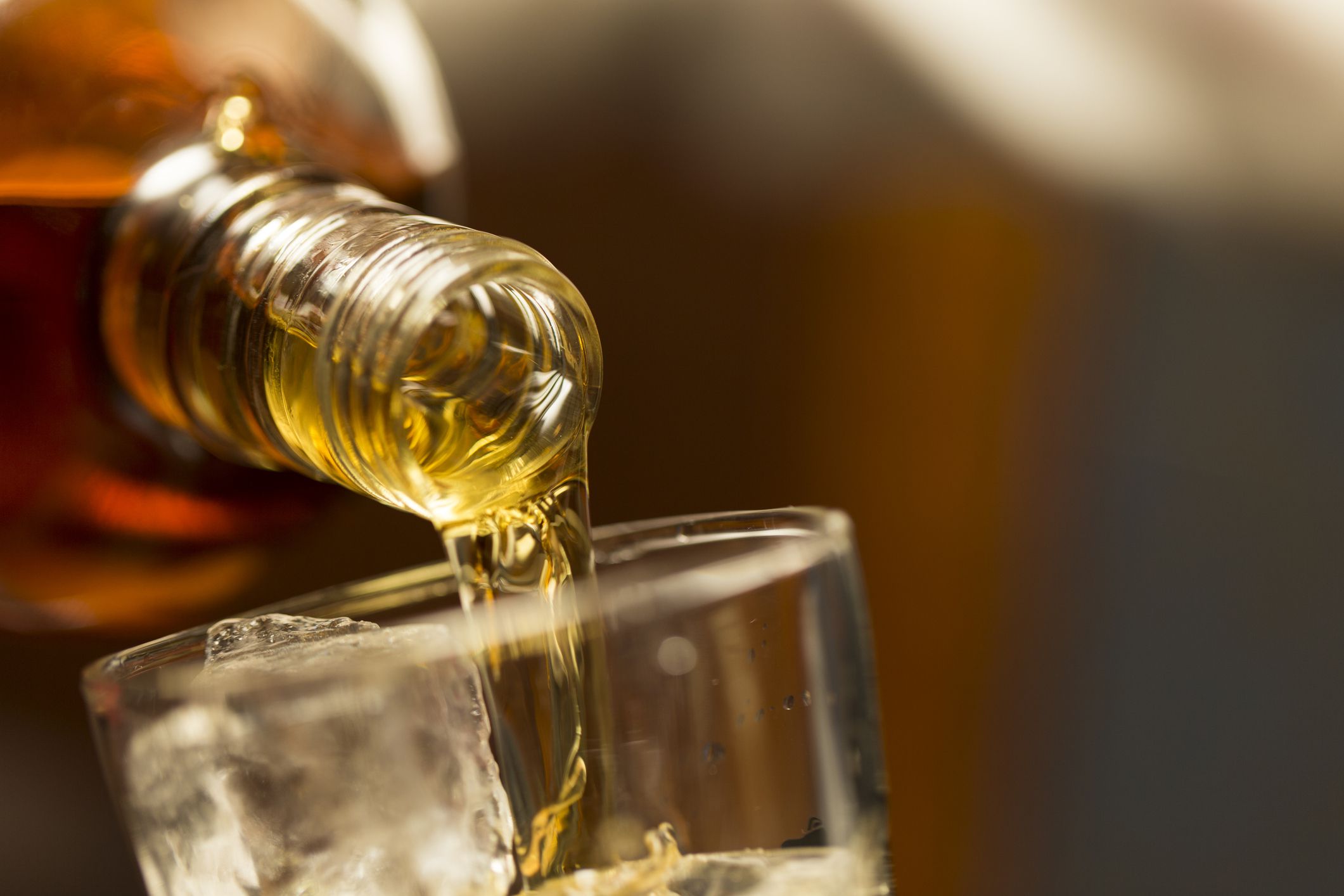 Pouring whiskey into a glass with ice.