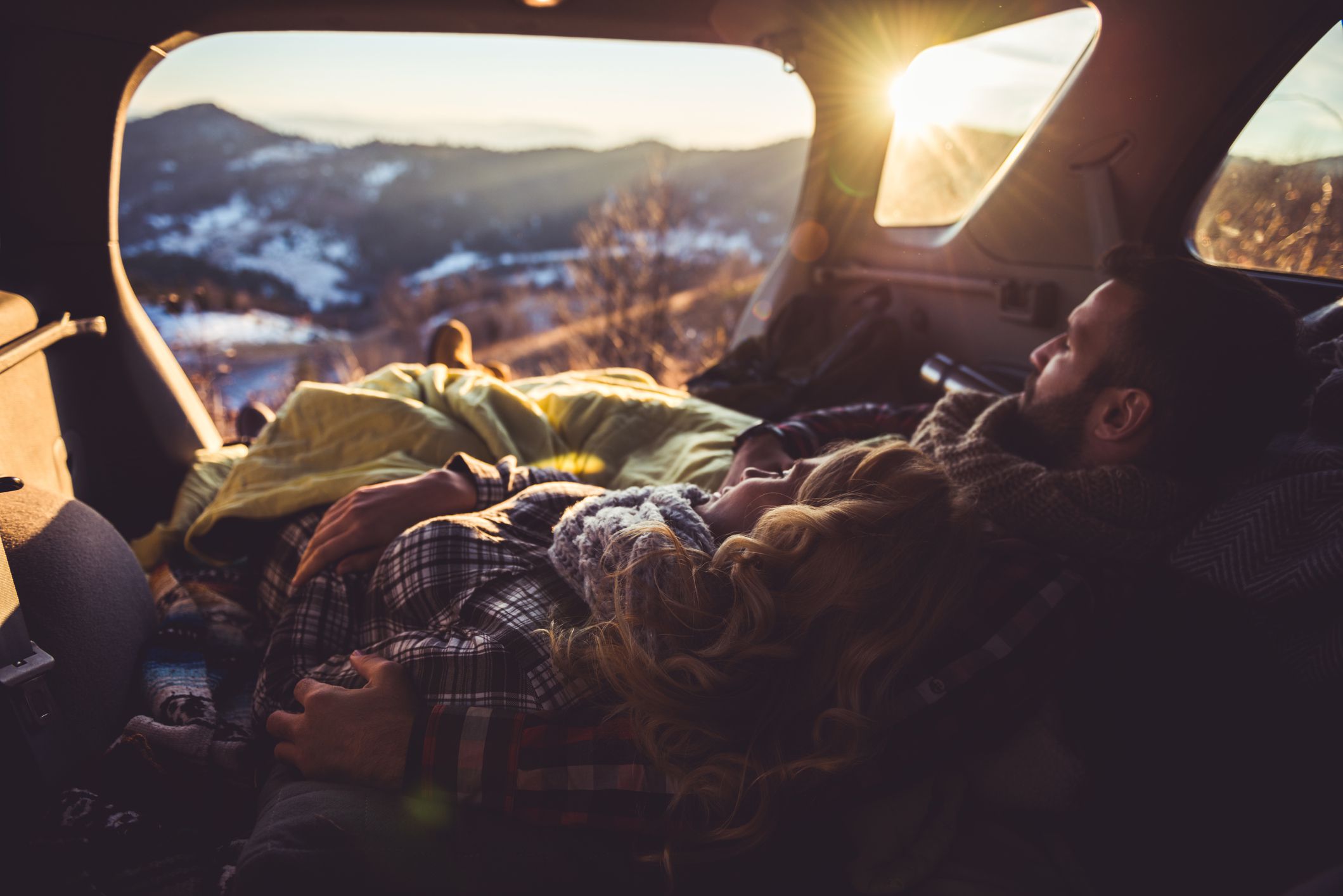Couple in love sleeping in a car trunk covered with blanket.