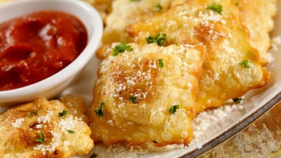 Golden fried ravioli, a delicious option for cheap appetizers, sprinkled with grated parmesan and parsley, served with marinara sauce for dipping—perfect for parties.