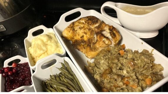A Thanksgiving meal featuring sliced roasted turkey, gravy, Costco Thanksgiving sides like stuffing, green beans, mashed potatoes, and cranberry sauce arranged in white serving dishes.
