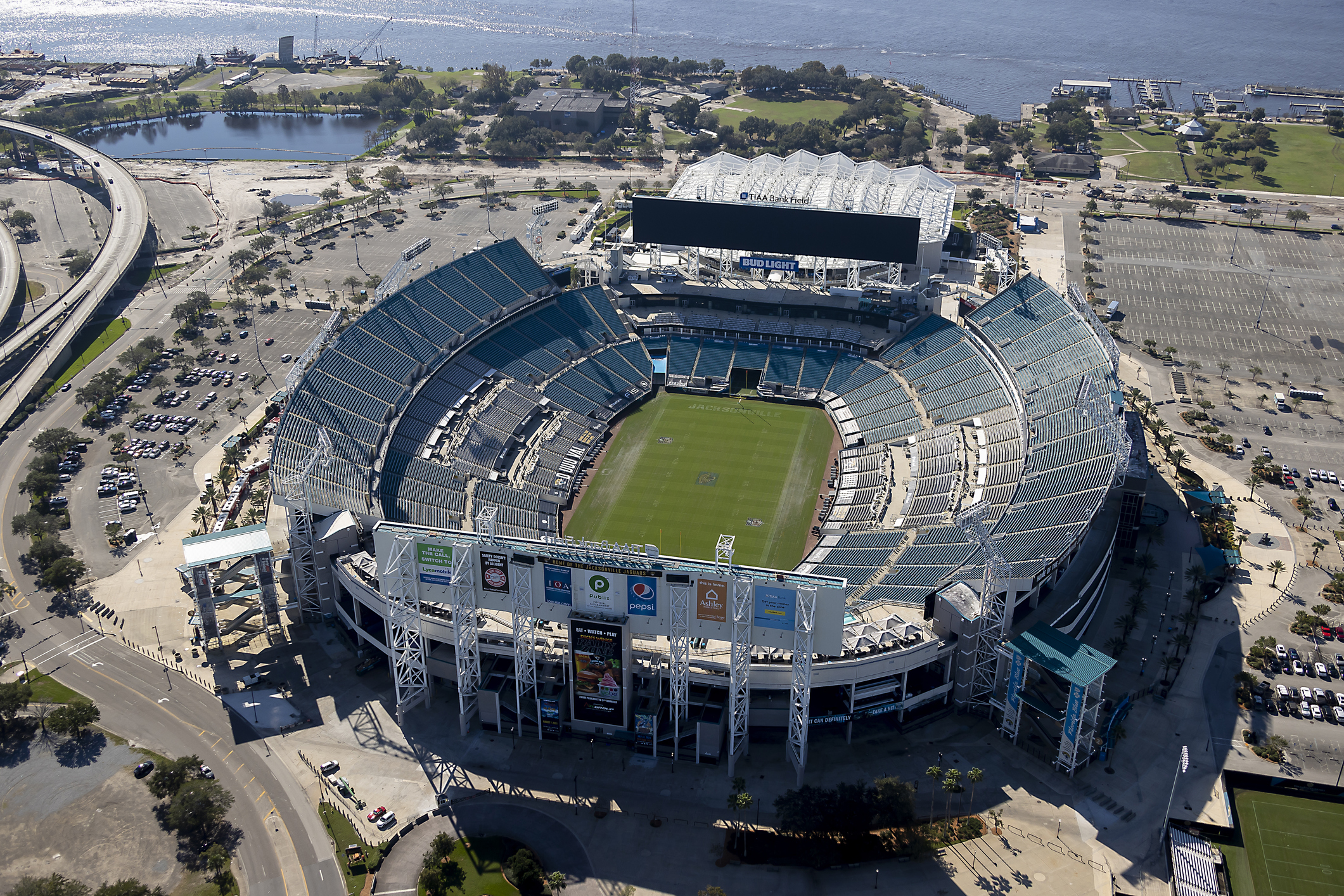 Aerial of an opened and empty field of Jacksonville Jaguars, TIAA Bank Field, Jacksonville, Florida on a sunny day, with the parking lot, highway, and river in the background