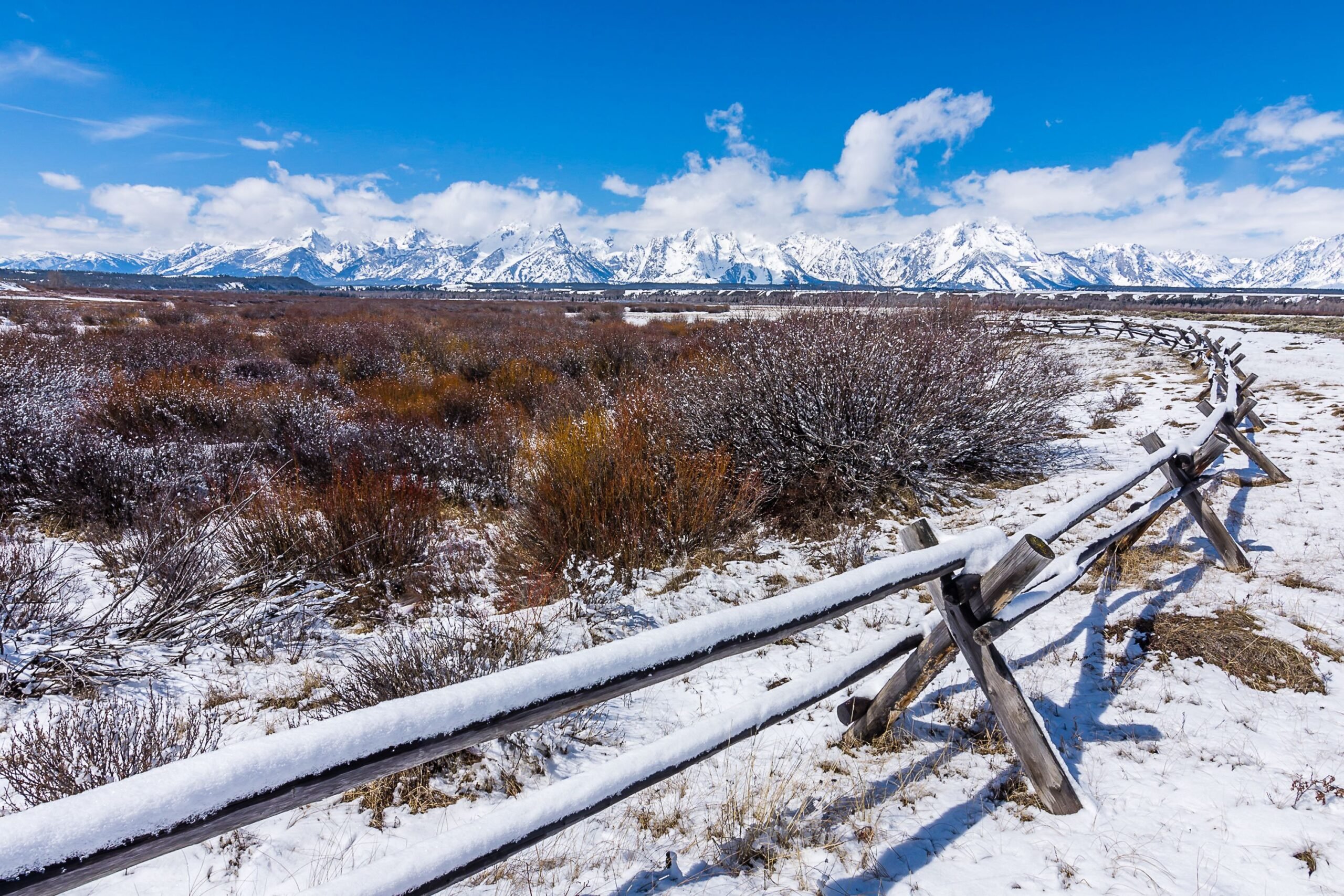Rustic wooden fence curling from the foreground towards the distance in Wind River Country, Wyoming during winter, with massive mountains in the background