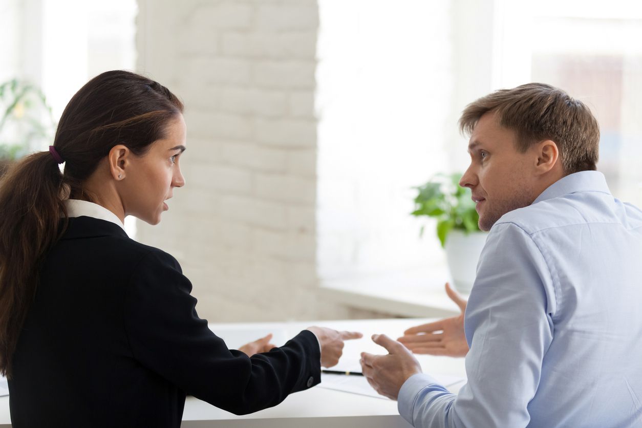 A man and a woman sitting in an office and arguing with each other.