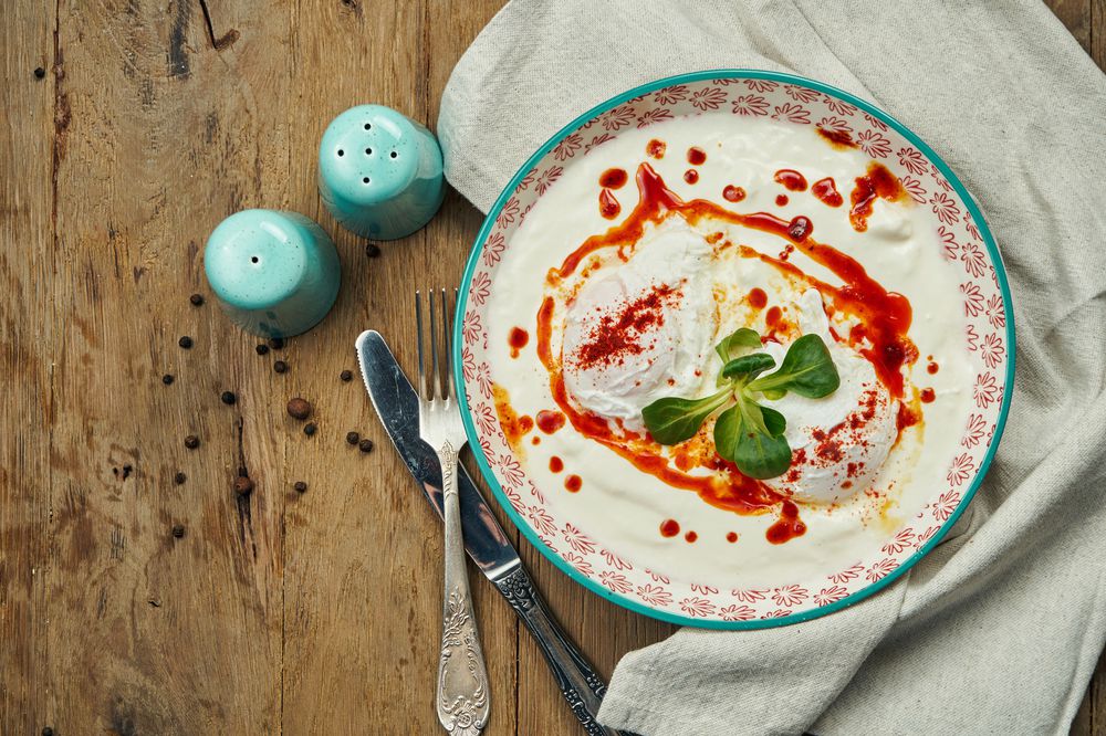 Healthy breakfast - poached egg with yogurt sauce in a blue bowl on a wooden background. Cilbir