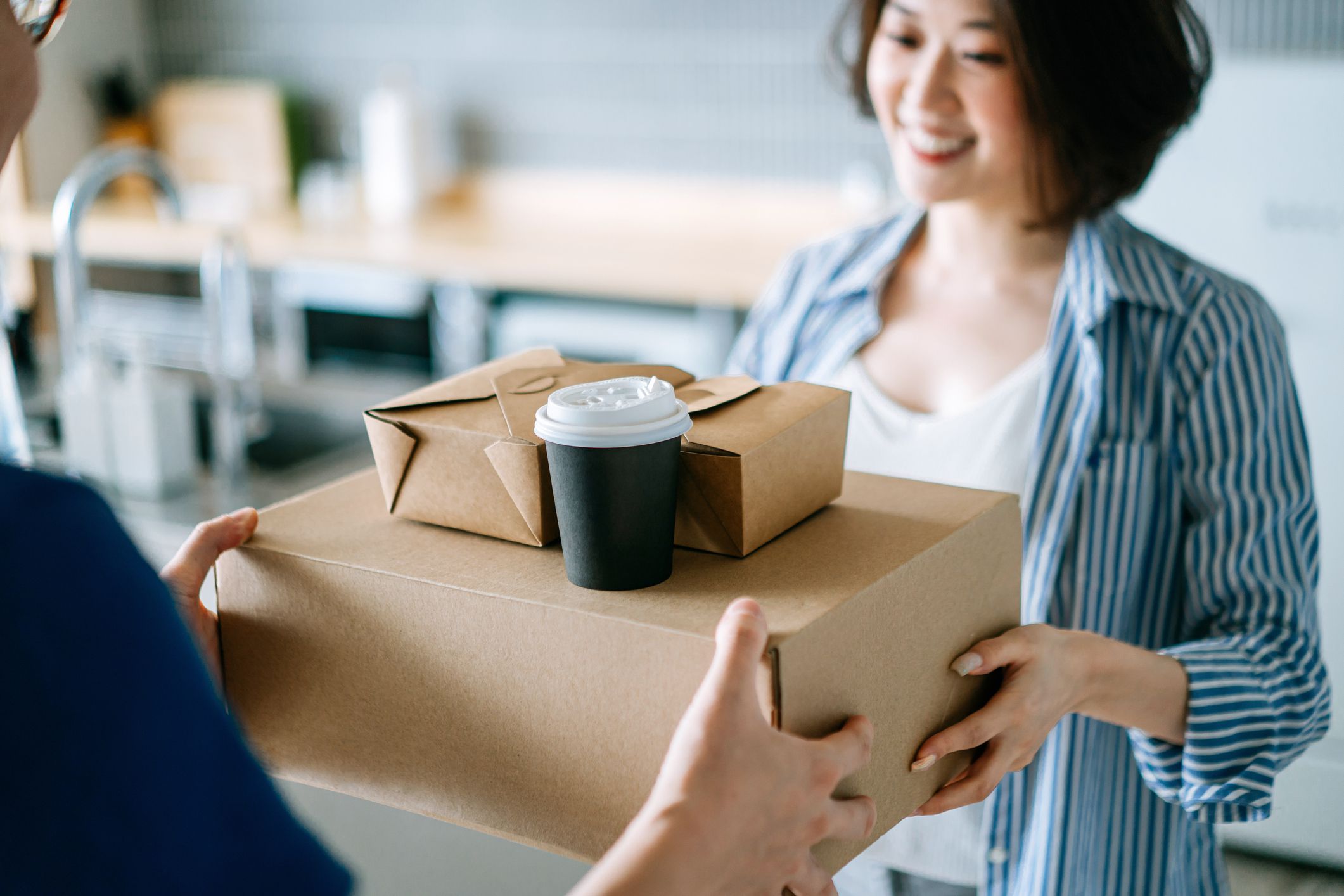 Close up of beautiful and cheerful young Asian woman receiving home delivery takeaway food order from a delivery man at home. Eating at home concept
