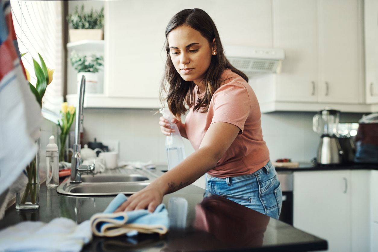 A young woman cleaning up the kitchen countertop.