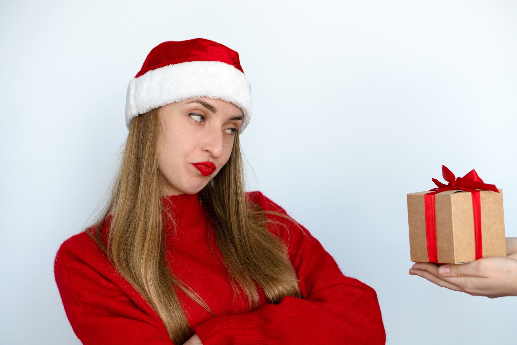 A beautiful girl dressed as Santa contemptuously looks at the gift. Christmas holidays.