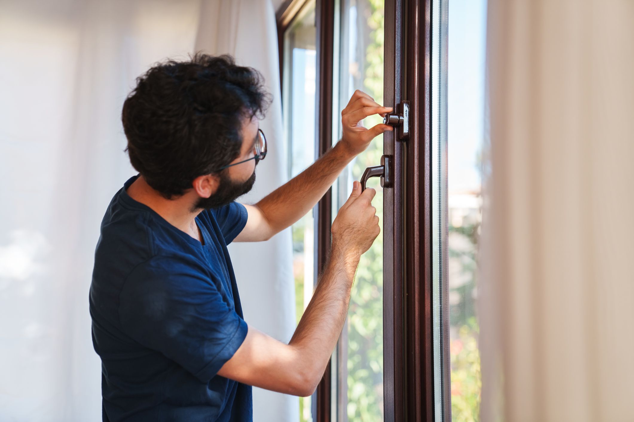 The young man is closing the lock on window for safety