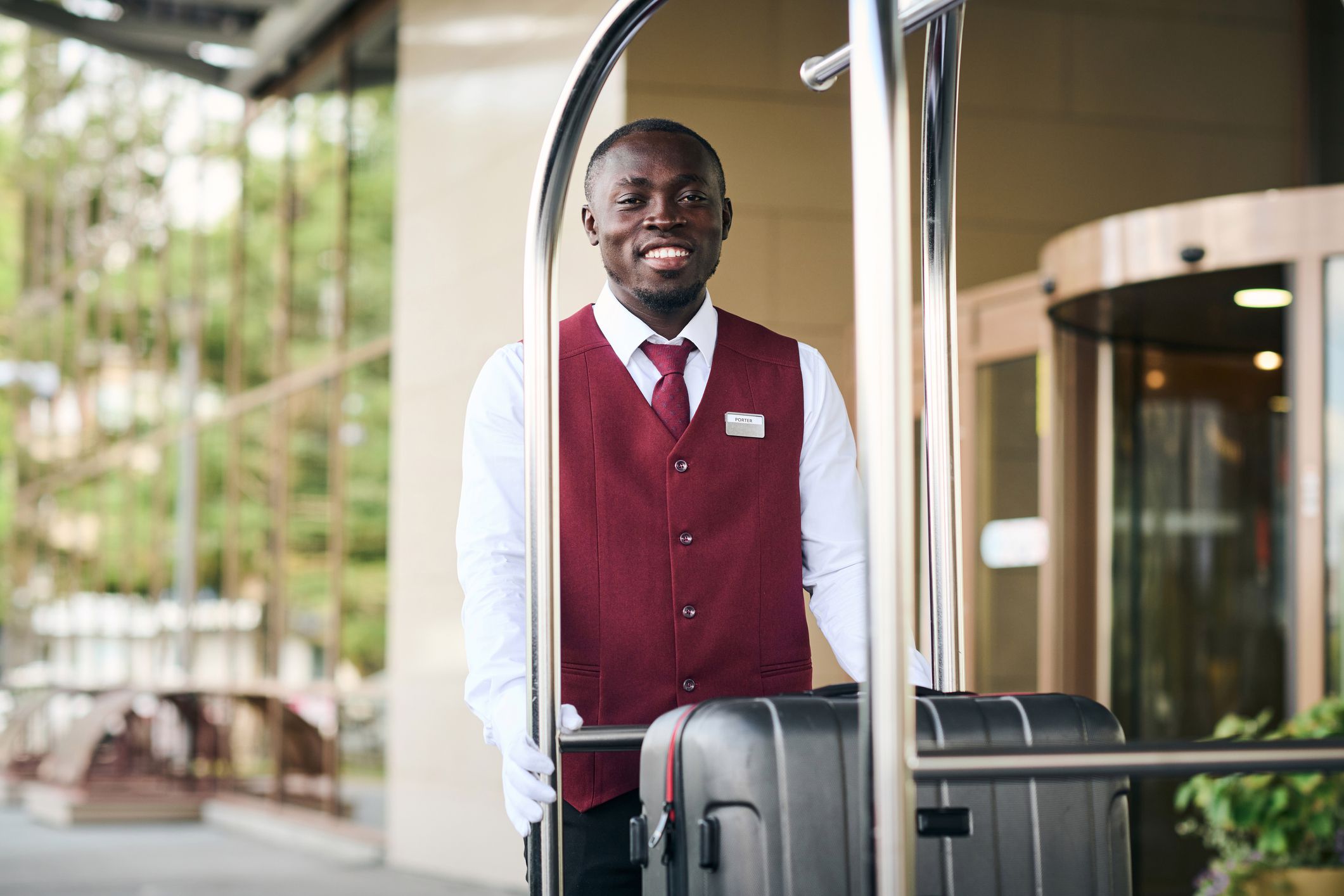 Portrait of African American doorman standing outdoors near the trolley with baggage and smiling at camera