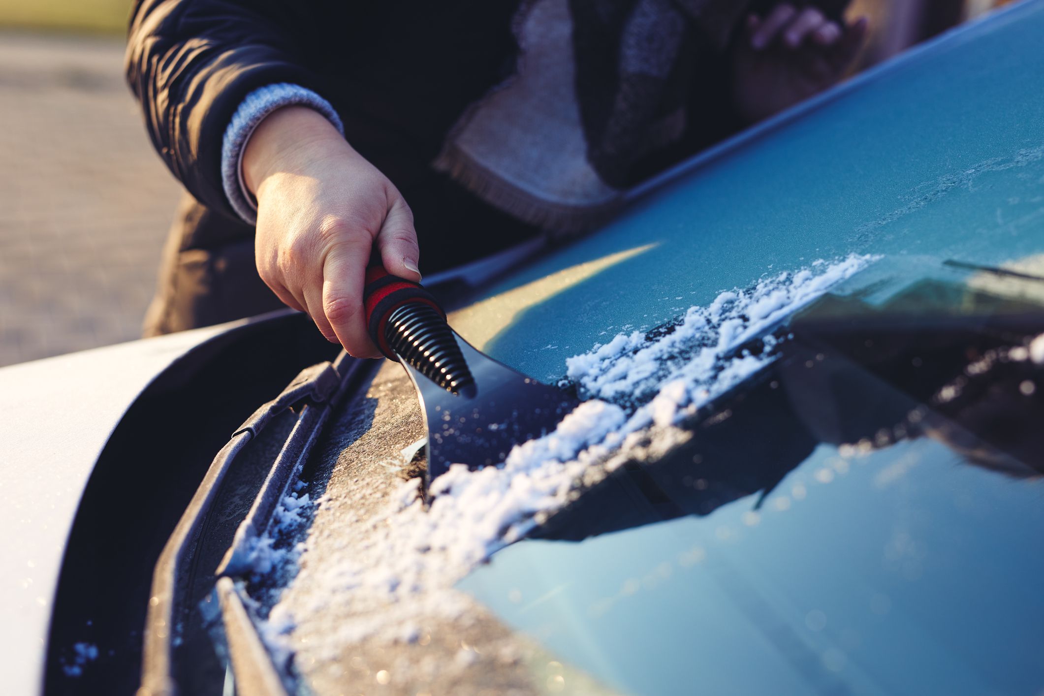 A woman scratches the front window of her car on a cold winter morning