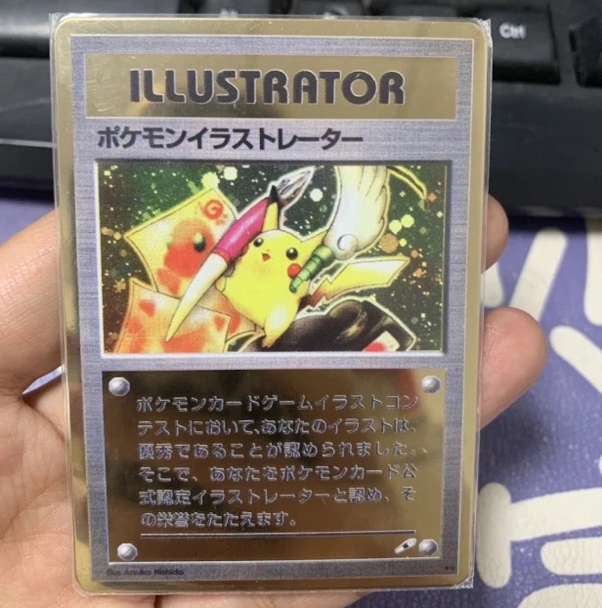 A hand holds a rare Pokémon Illustrator card—one of the most expensive collectibles—featuring Pikachu with a pen and drawing tools, accented by Japanese text and vibrant yellow, green, and red hues in the background.