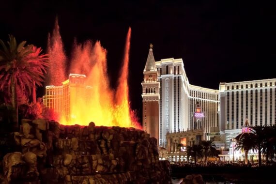 The Mirage volcano erupting with fire and water at night, with The Venetian hotel visible in the background.
