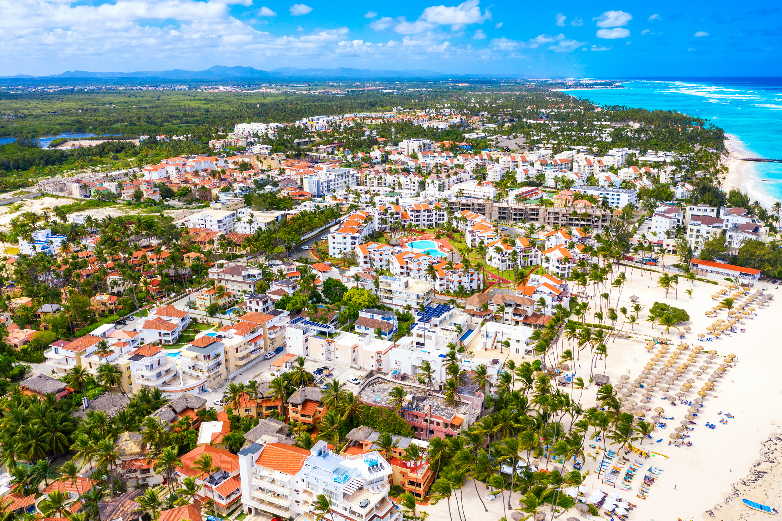 Aerial of numerous hotels and condos in Bavaro, Punta Cana, Dominican Republic, beach on the right, mountains in the distance, on a sunny day