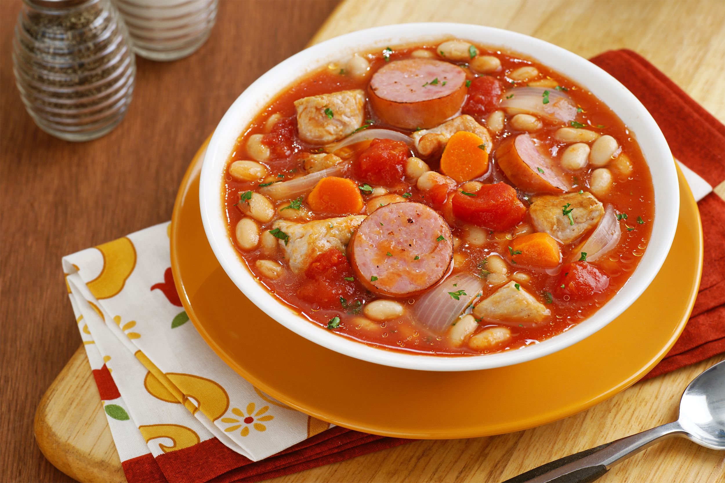 Bean and Sausage Soup in white bowl on yellow plate on wood table