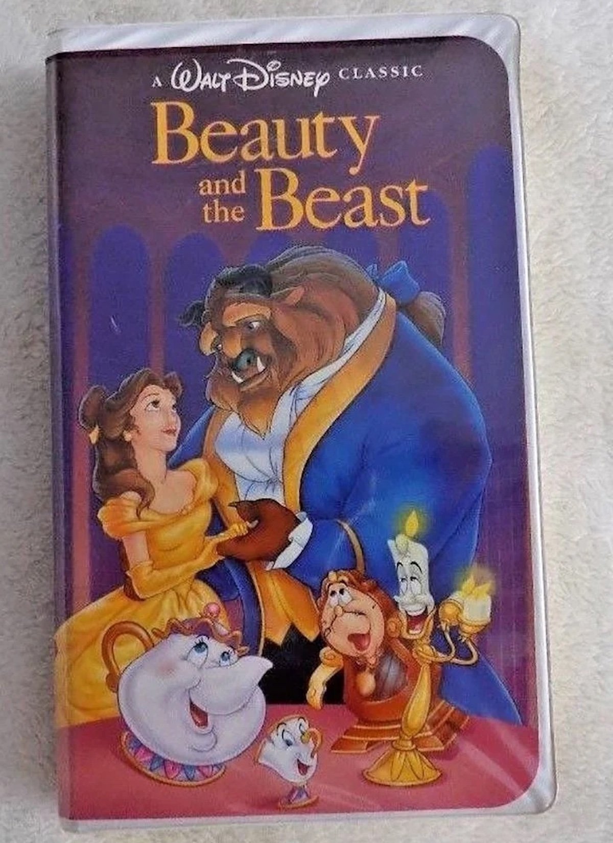 A VHS tape cover of Disney’s “Beauty and the Beast,” an example of expensive collectibles, featuring Belle, Beast, Mrs. Potts, Chip, Cogsworth, and Lumière smiling together in a warmly lit, elegant setting.