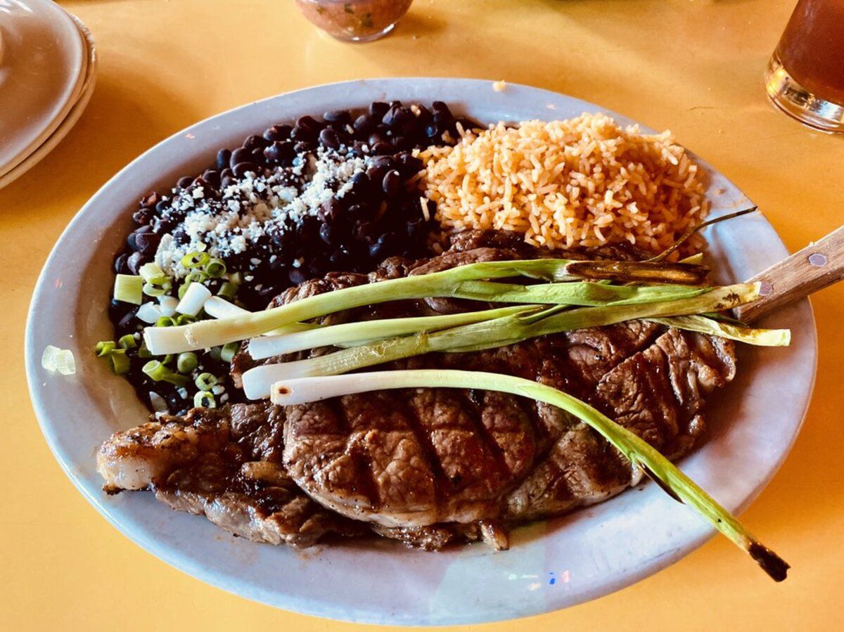 Carne Asada on a white plate, El Coyote, Los Angeles, with a drink and a condiment on a yellow-orange table at the restaurant