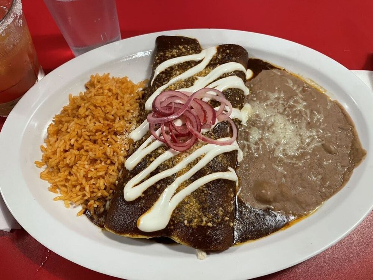 Enchiladas de Mole on a white plate with a glass of water and a margarita, Acapulco, Alameda, California, on a red table in the restaurant