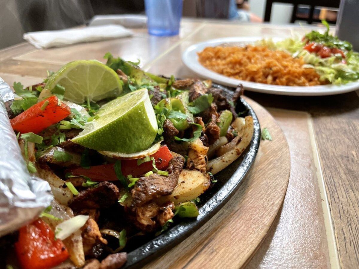 Closeup of Chicken & Steak Fajita on a cast iron serving plate with wooden holder, El Castillo Taqueria & Bakery, Jacksonville, Florida, selective focus, another dish on a white plate in the background, all on a table at the restaurant blurred