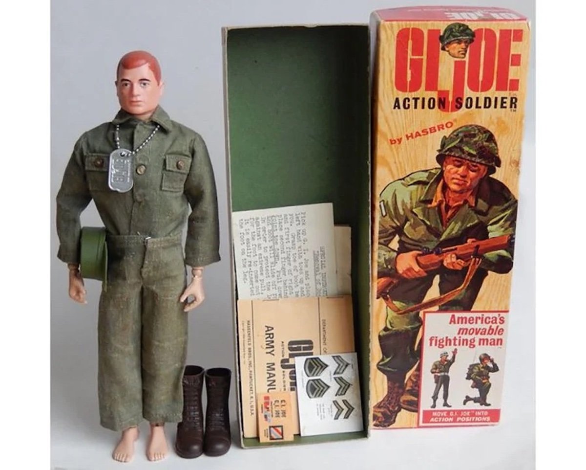 A vintage G.I. Joe action soldier doll stands beside its original box, with accessories including boots, dog tags, and paperwork—an excellent find for fans of expensive collectibles. The box features artwork of a soldier and “G.I. JOE Action Soldier.”