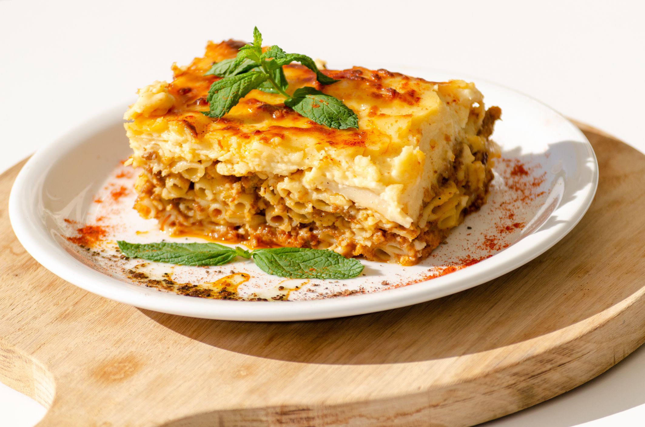 Greek beef pasta bake, Pastitsio, on a white porcelain plate, on a serving wooden board, with a white background