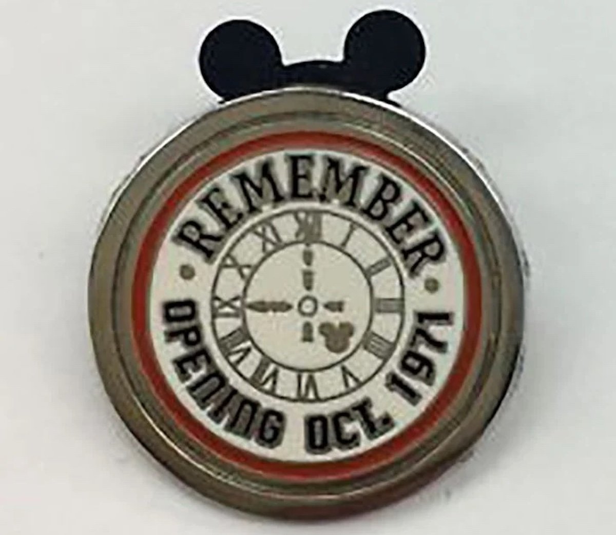A round pin with Mickey Mouse ears, featuring a clock face with Roman numerals, the word "REMEMBER" at the top, and "OPENING OCT. 1971" around the edge—one of the most sought-after expensive collectibles for Disney fans.