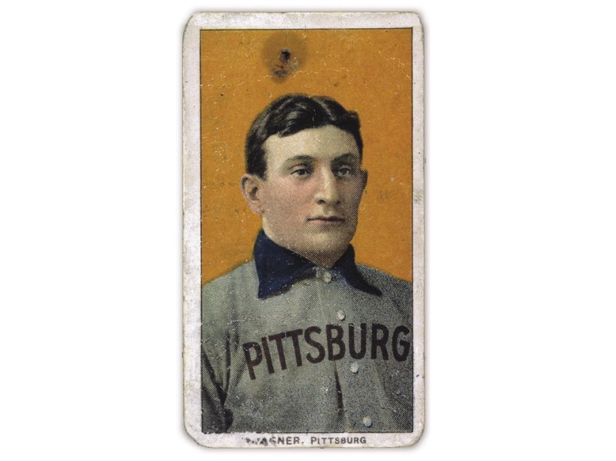 A vintage baseball card, considered one of the most expensive collectibles, shows a man with short dark hair in a gray and blue "PITTSBURG" uniform against an orange background. The card features worn edges and visible signs of aging.