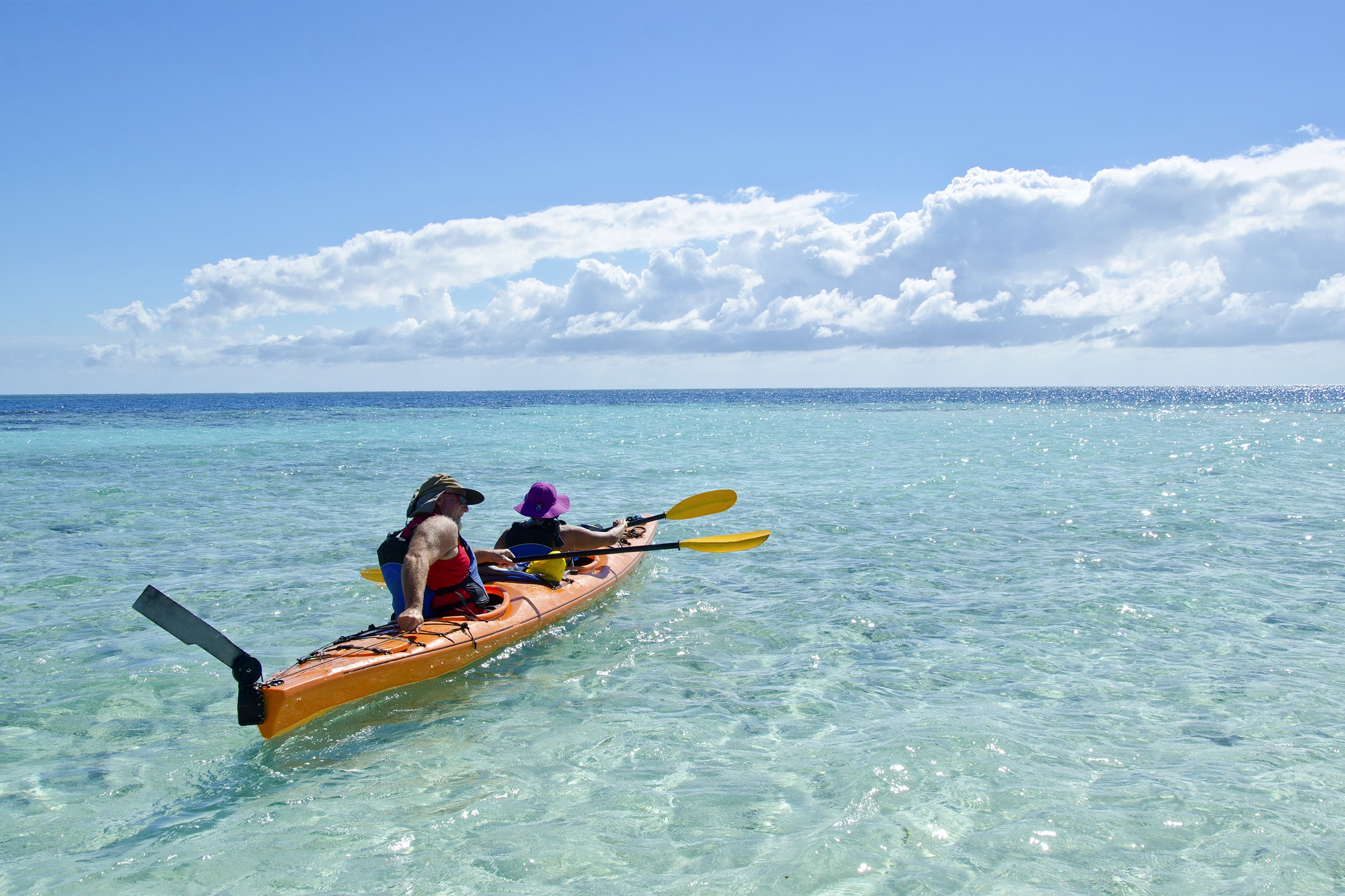 A man and a woman embark in a sea kayak near the Barrier Reef, Caribbean Sea, Belize, kayak on the left, clear water, ocean on the horizon, blue sky with white clouds