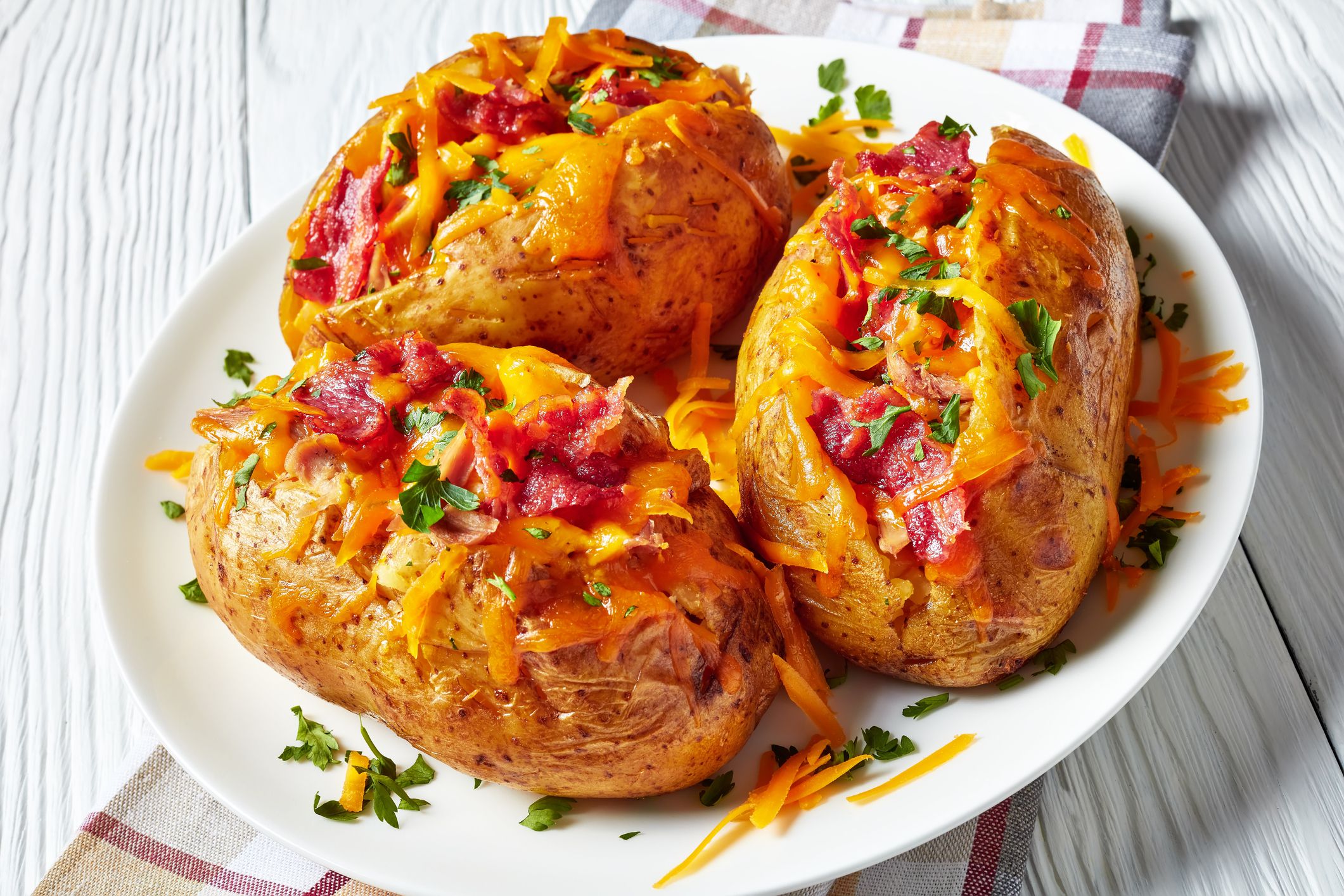Loaded freshly Baked hot Potatoes with crispy fried Bacon, pulled chicken breast and melted cheddar cheese on a white plate on a wooden table, view from above, close-up
