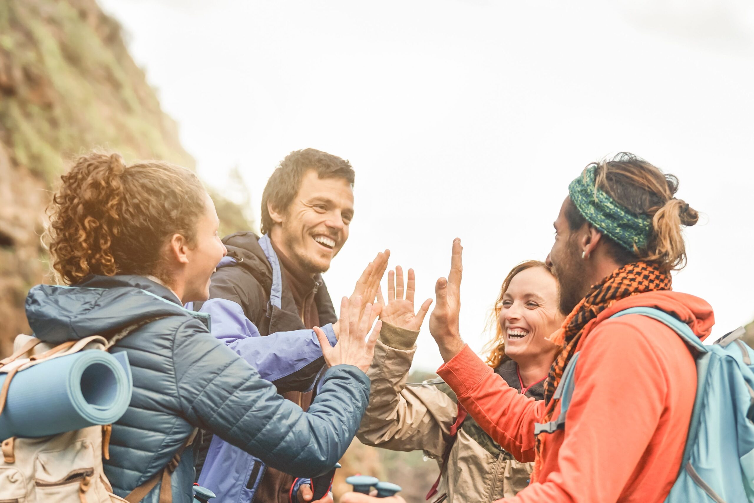 Group of friends stacking hands while doing trekking excursion on mountain - Young tourists having fun exploring the wild nature - Trekker, team, hike and travel people concept