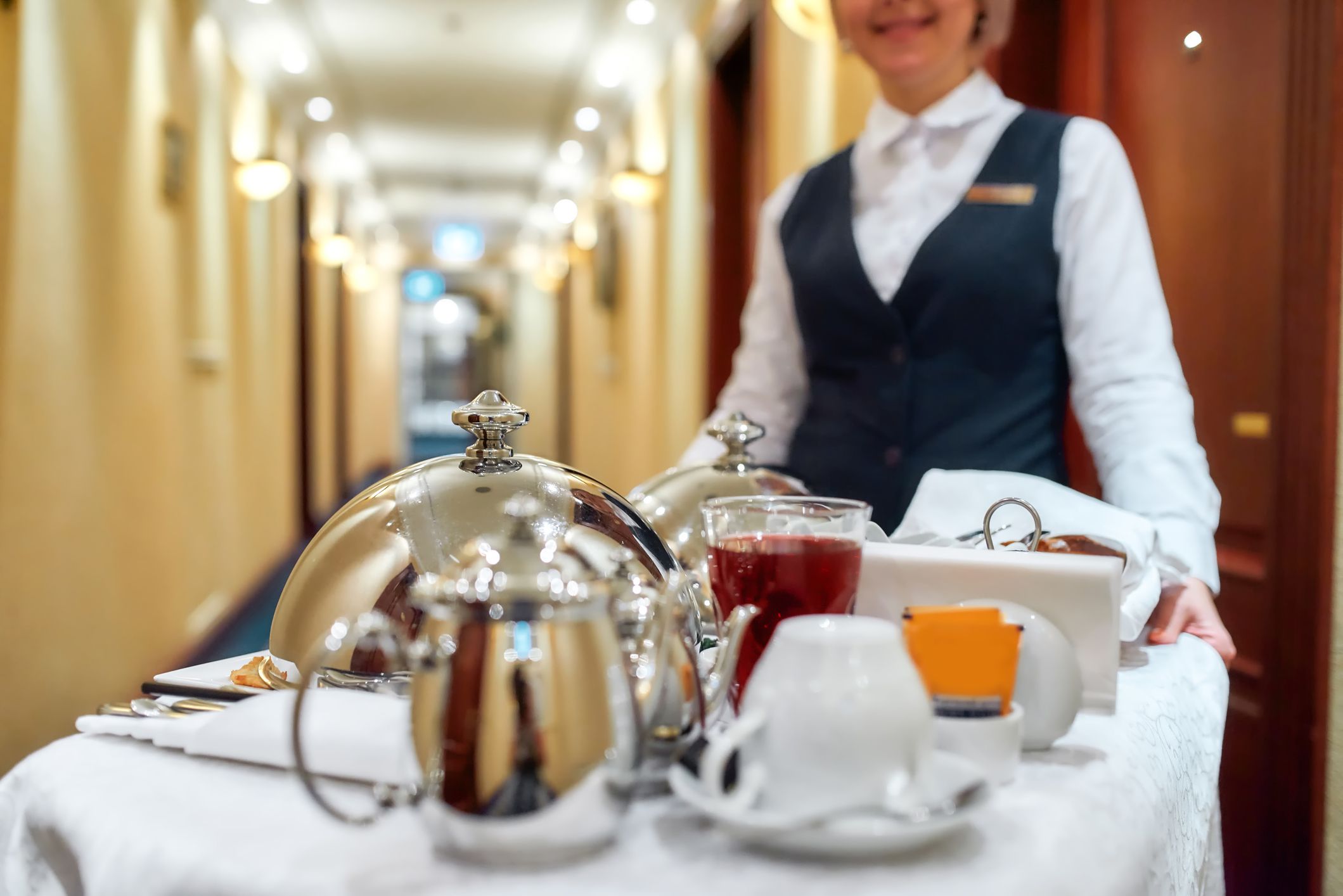 Waitress in uniform delivering tray with food in a room of hotel. Room service. Selective focus on tableware. Horizontal shot