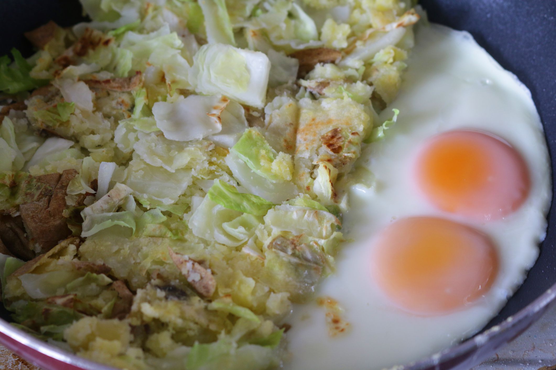Stock photo showing an elevated view of a non-stick pan containing homemade bubble and squeak made from mashed potatoes, onions, white cabbage and served with two fried eggs.