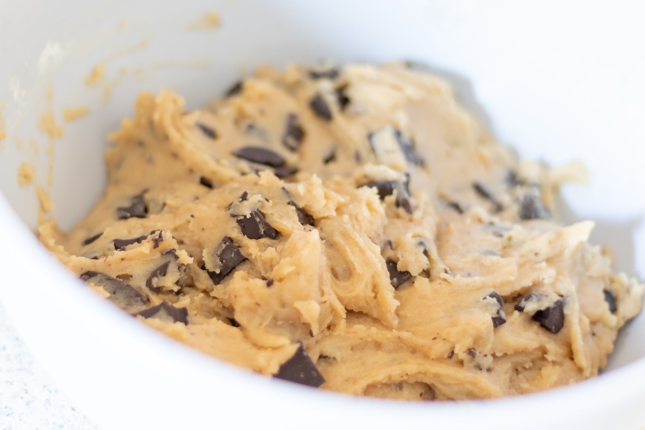 Homemade cookie dough with chocolate chunks being mixed in a bowl on a counter.