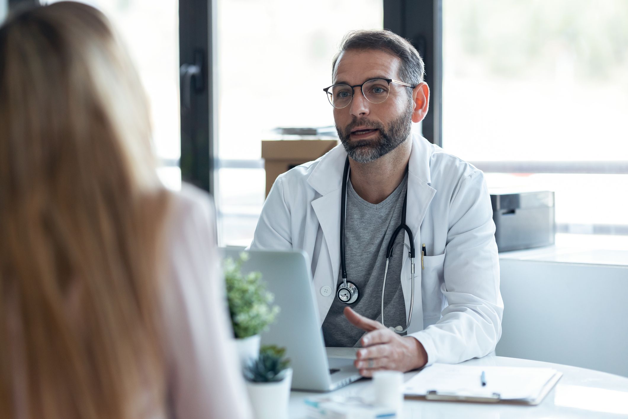 Shot of handsome mature male doctor talking while explaining medical treatment to patient in the consultation.