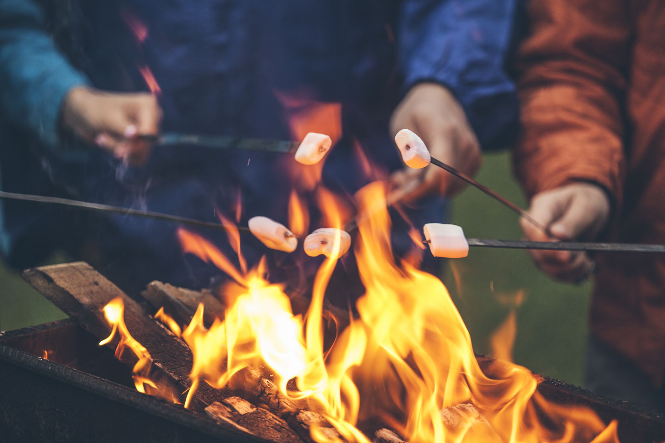 Hands of friends roasting marshmallows over the fire in a grill closeup