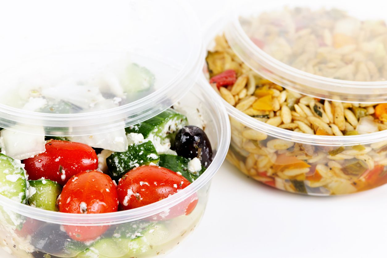 A couple of food containers filled with pasta and a salad.