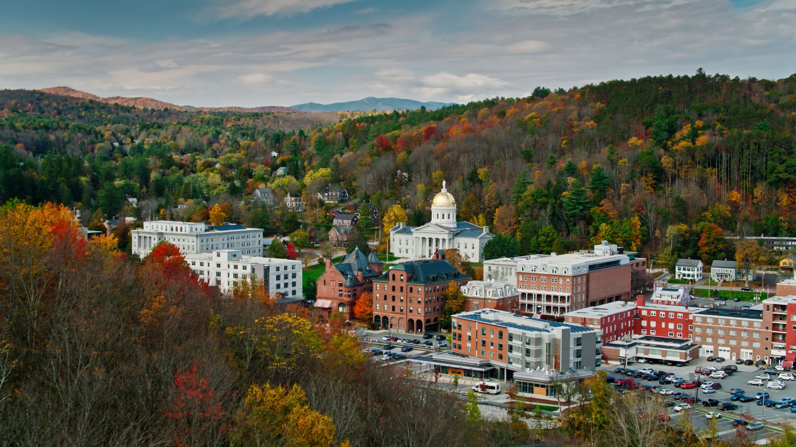 Aerial shot of the state capitol building in Montpelier, Vermont in Fall, flying over downtown buildings with a mountainside covered in colorful autumnal trees behind. Authorization was obtained from the FAA for this operation in restricted airspace.