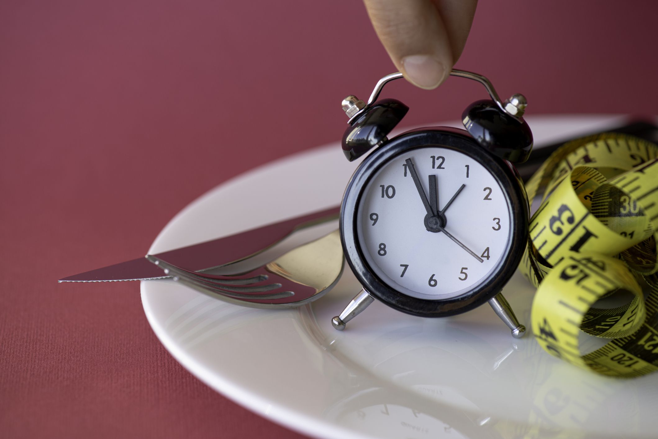 Measuring tape in empty plate with alarm clock. Woman holding alarm clock.