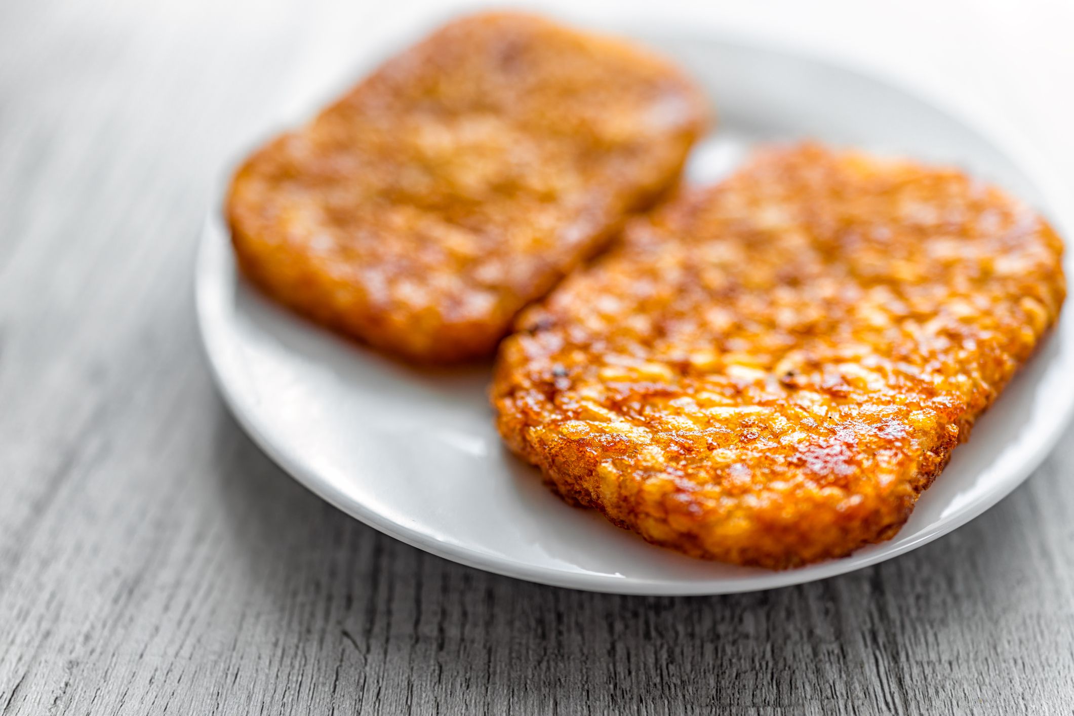 Macro closeup of breakfast or brunch potato fried two hash browns crispy texture on white plate with wooden table background