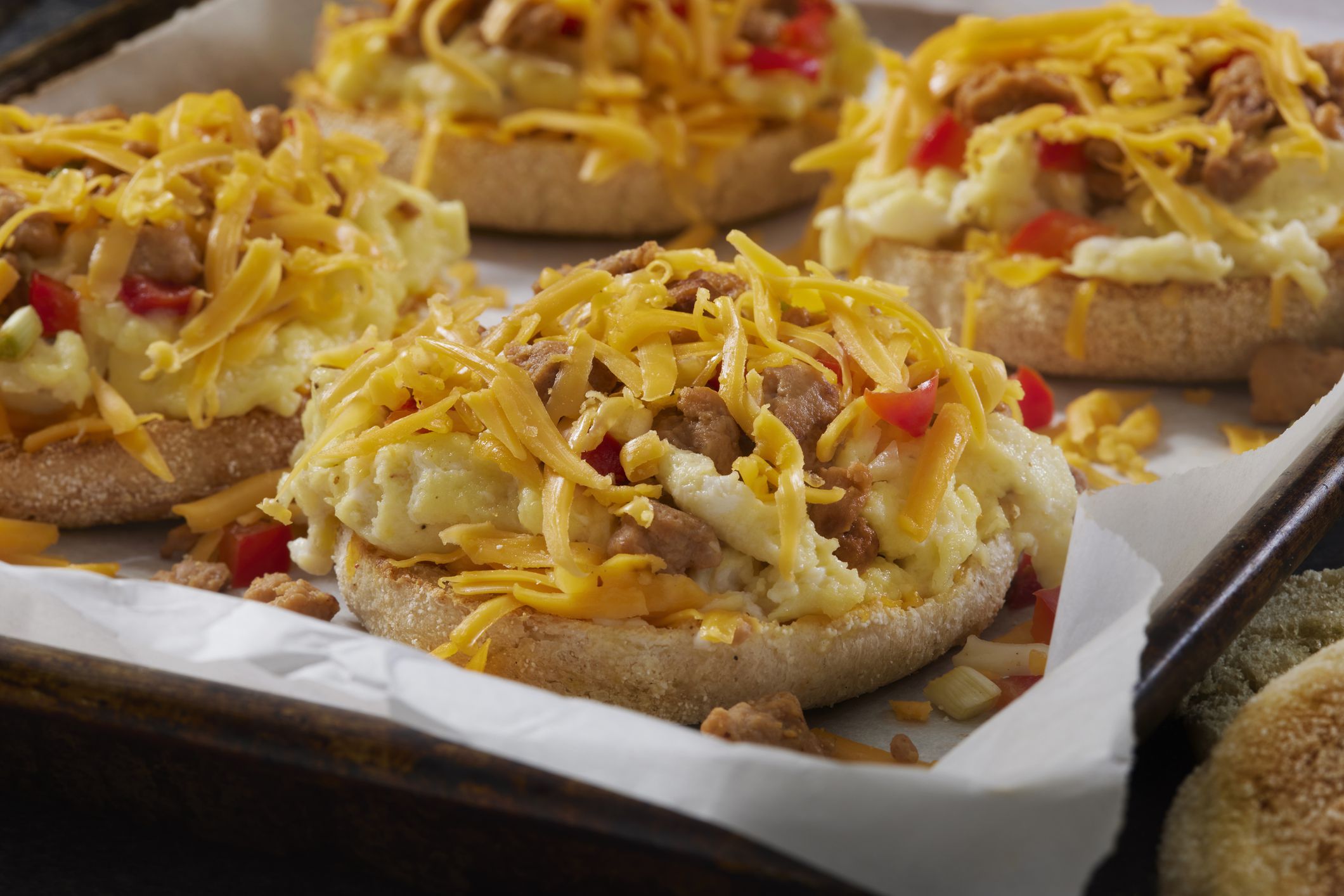 Preparing English Muffin Breakfast Pizza with Scrambled Eggs. Sausage and Peppers