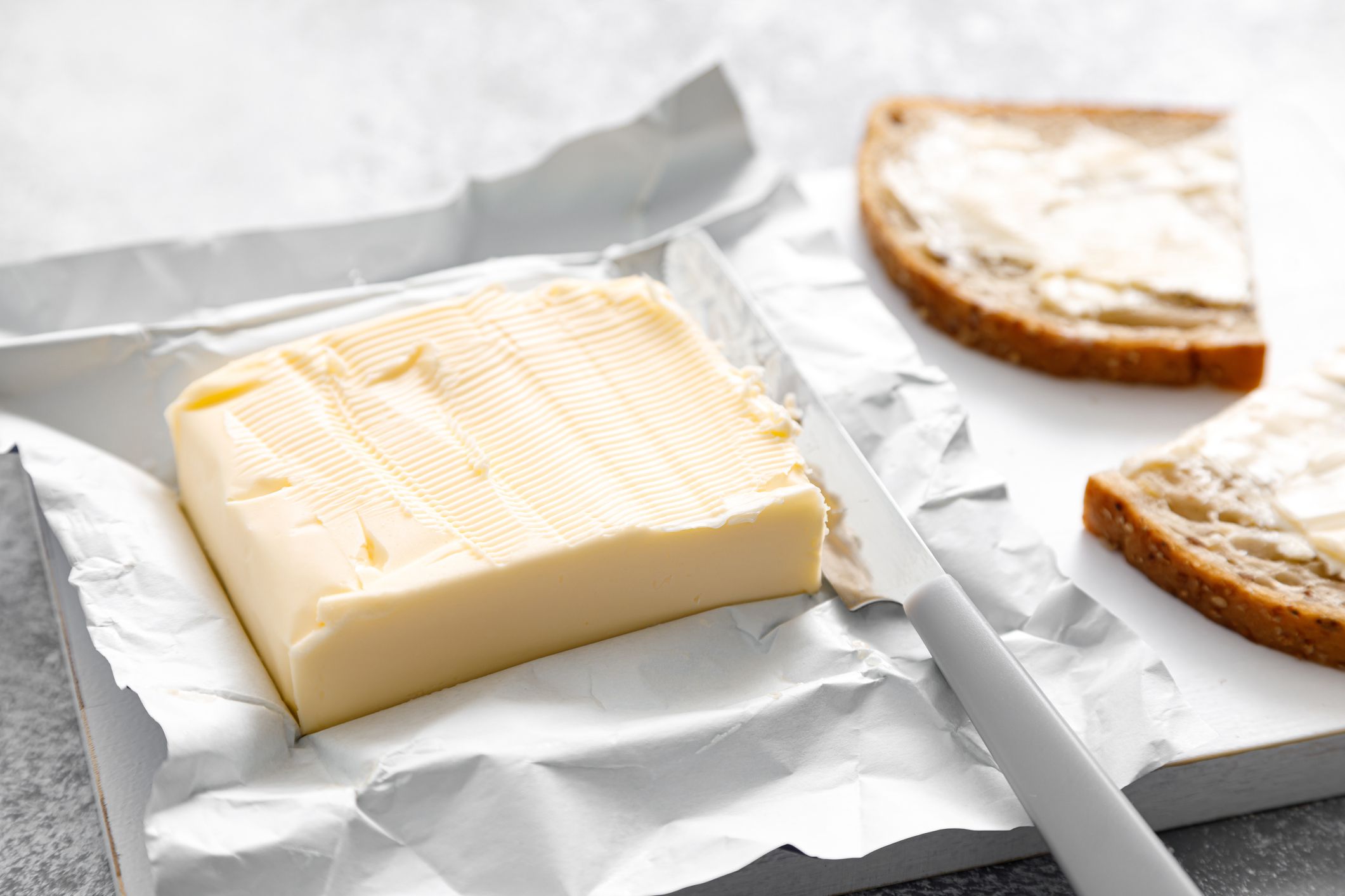 Block of butter with butter knife in a open pack. Buttering bread
