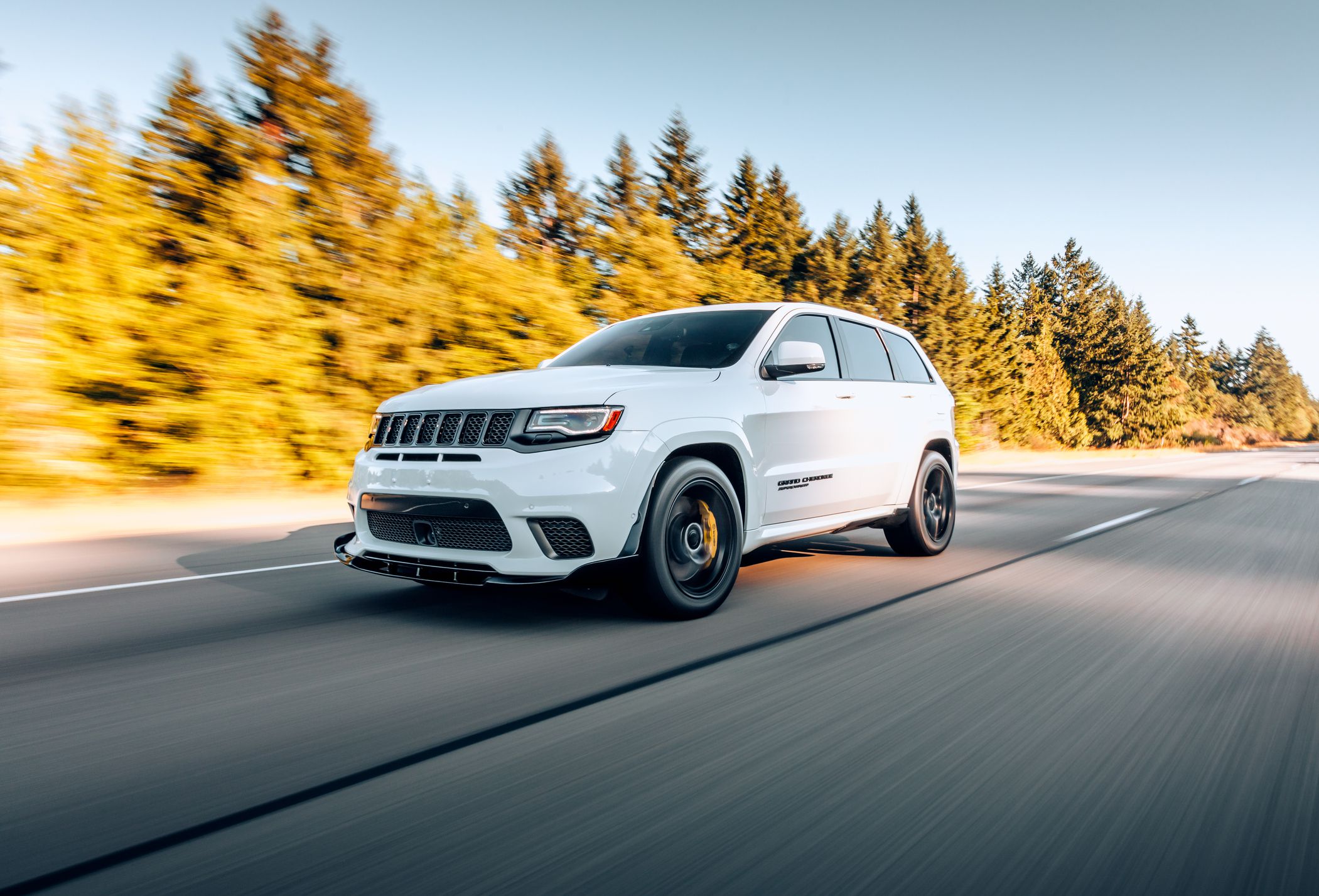 Renton, WA, USA4/19/2022White Jeep Grand Cherokee driving on the street with fir trees in the background