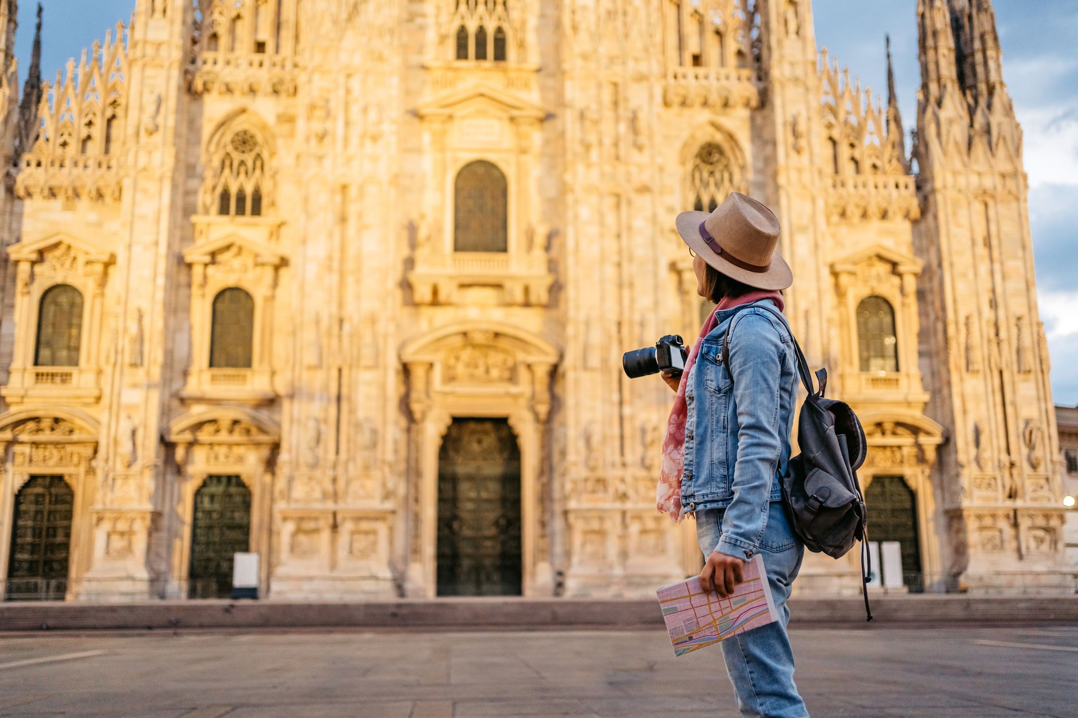 Beautiful young female tourist taking a picture of the cathedral in Milan, Italy, using camera.