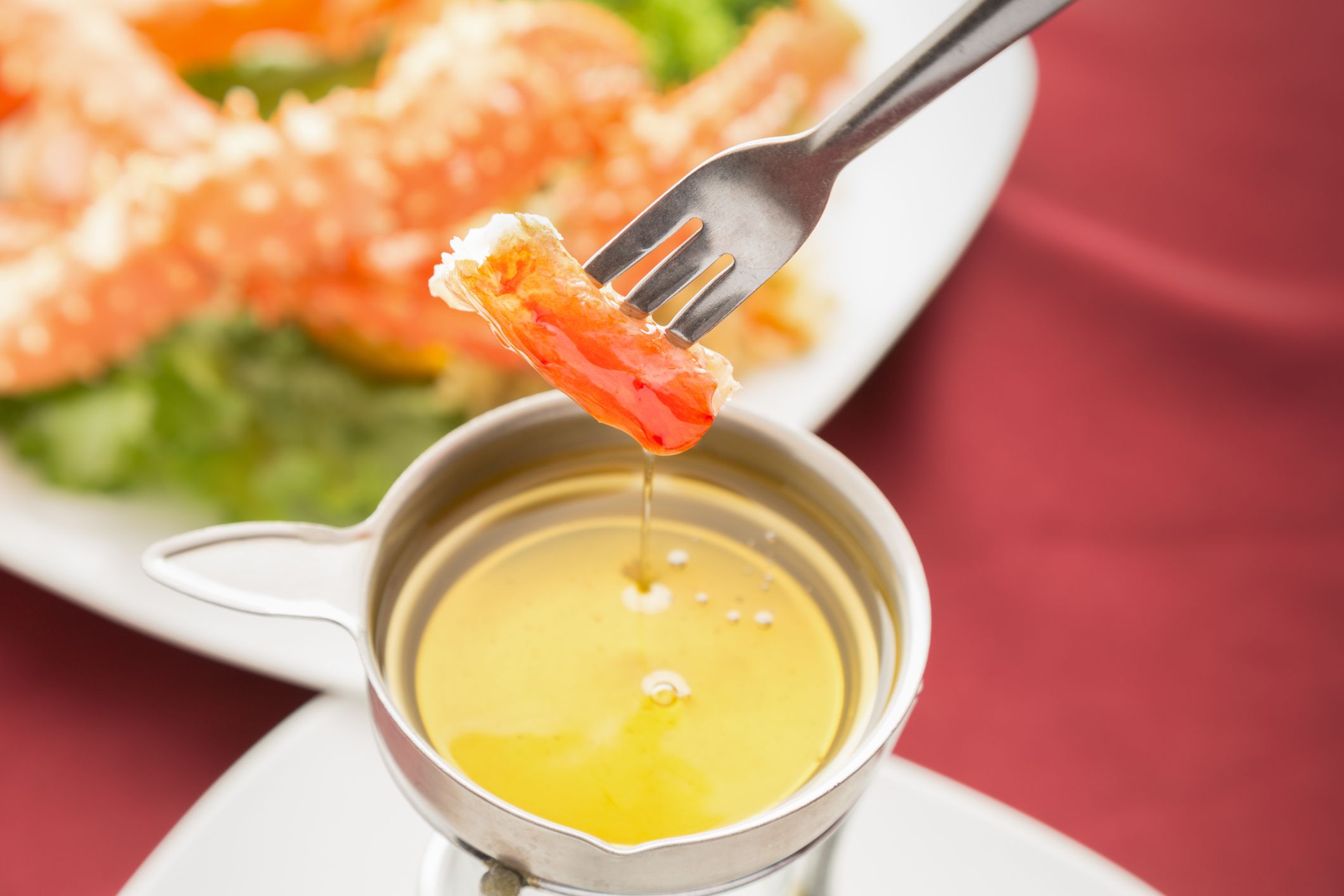King Crab Dipped in Clarified Butter with a plate of crab blurred in the background