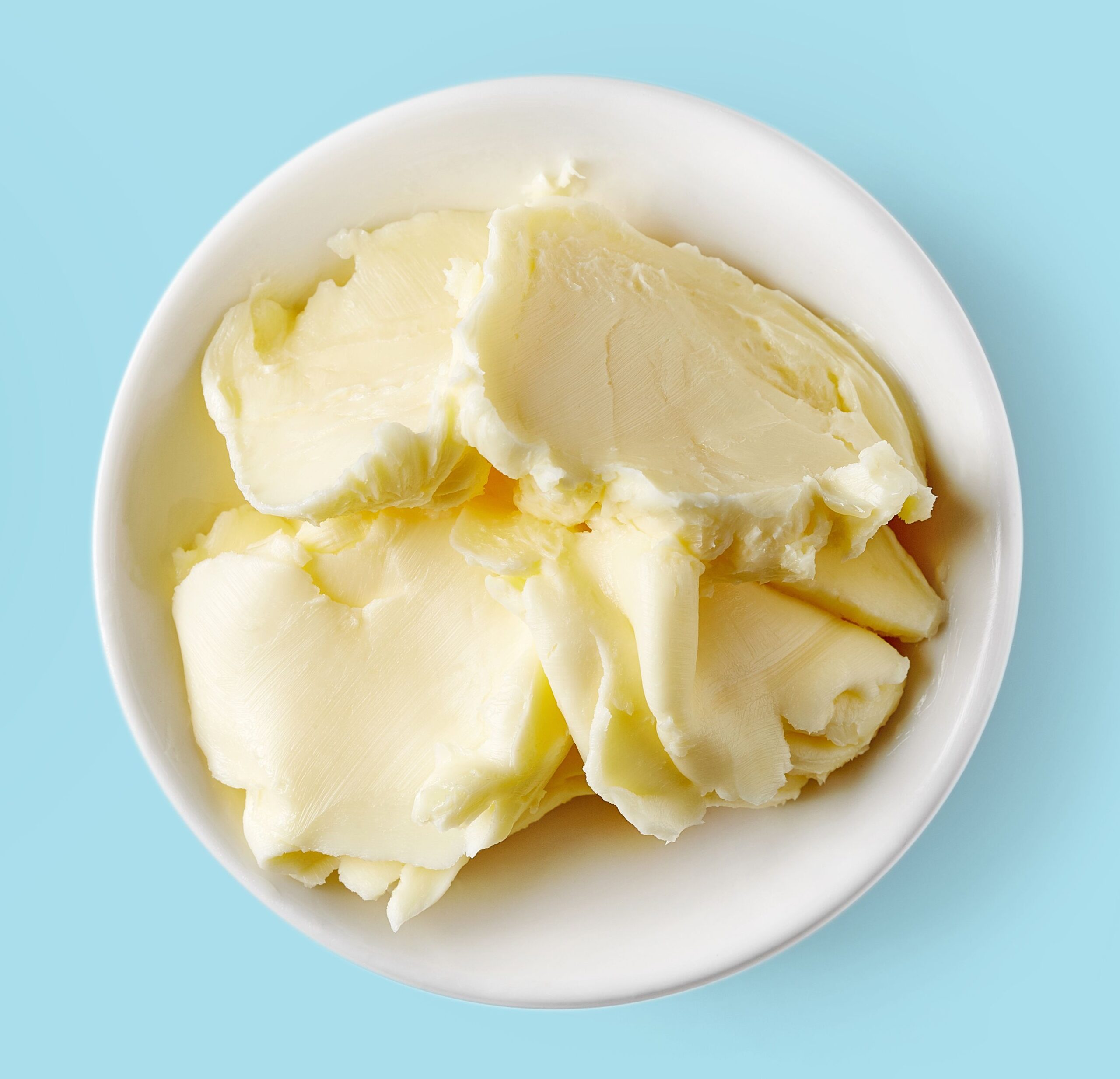 Bowl of butter on light blue background, top view