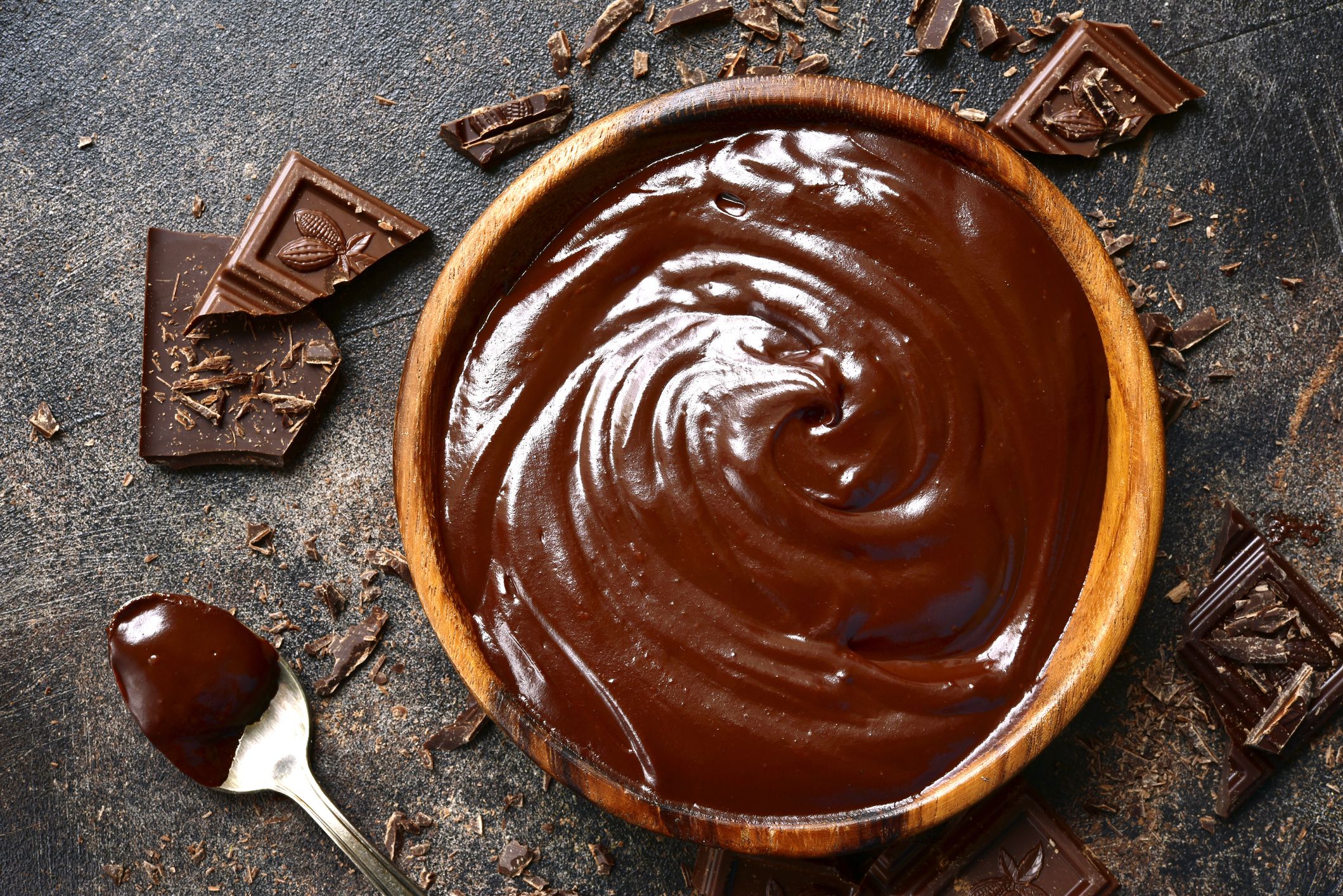 Chocolate ganache in a wooden bowl on a dark slate or rusty metal background.Top view with copy space.