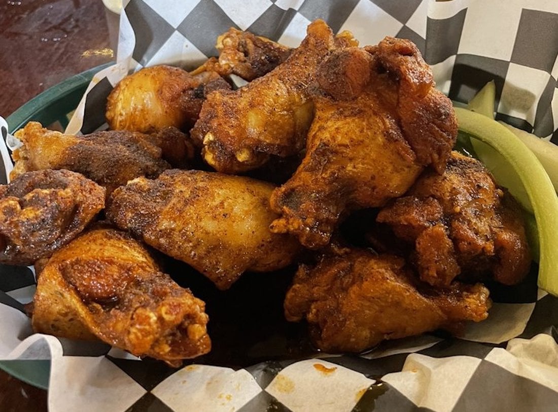 A basket of the best chicken wings, crispy and golden, is served on checkered paper with a few celery sticks on the side.