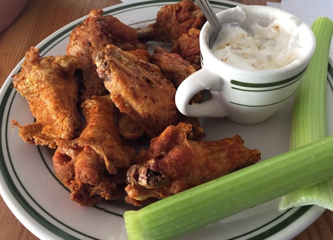 A plate of the best chicken wings, fried to crispy perfection, served with two celery sticks and a small cup of creamy dipping sauce—ranch or blue cheese—set on a table.