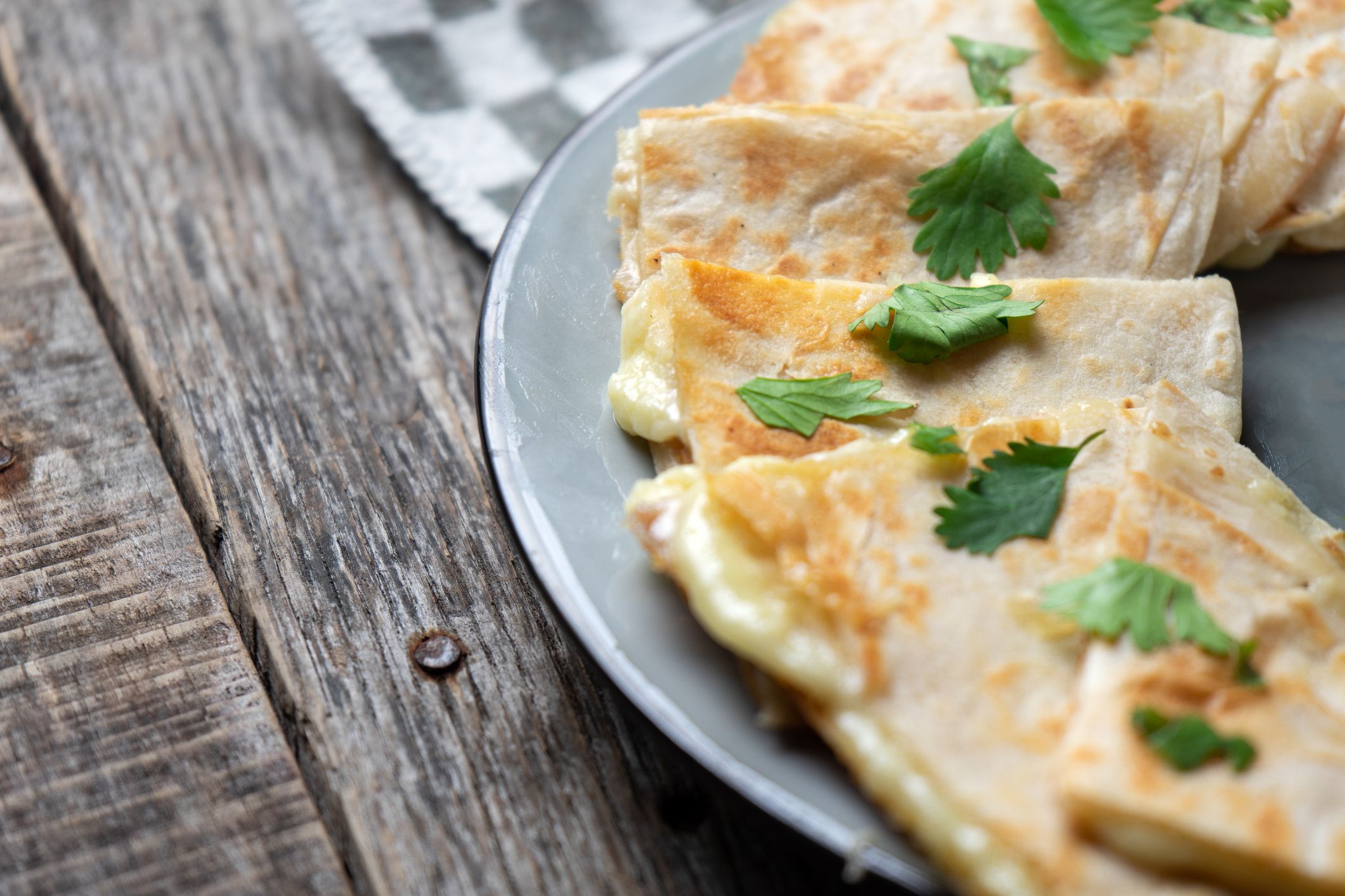 Classic cheese quesadillas in a circle on a grey plate on a black and white checkered napkin on a wooden table