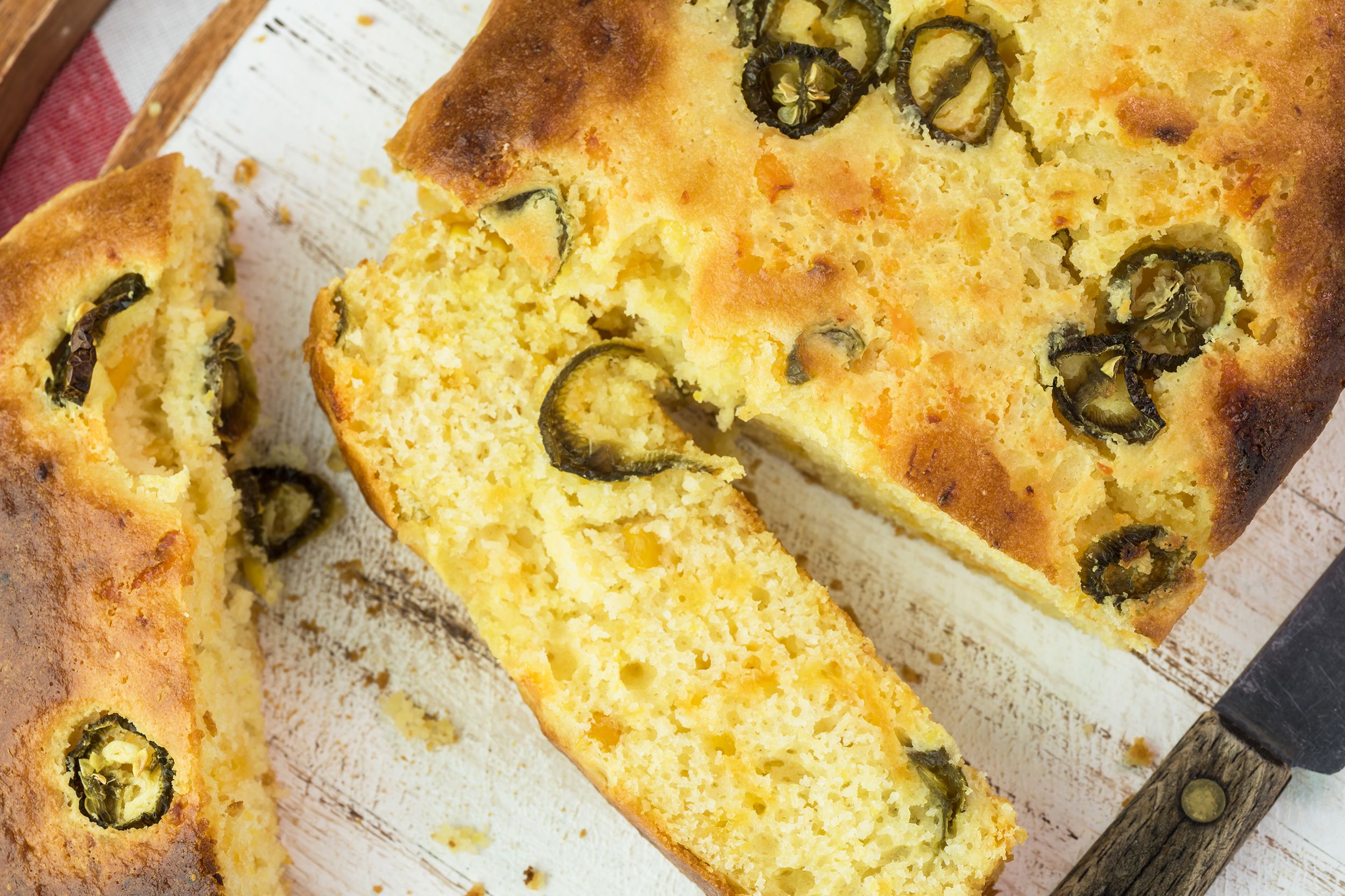 Closeup of a jalapeño cornbread loaf being cut with knife on a white board