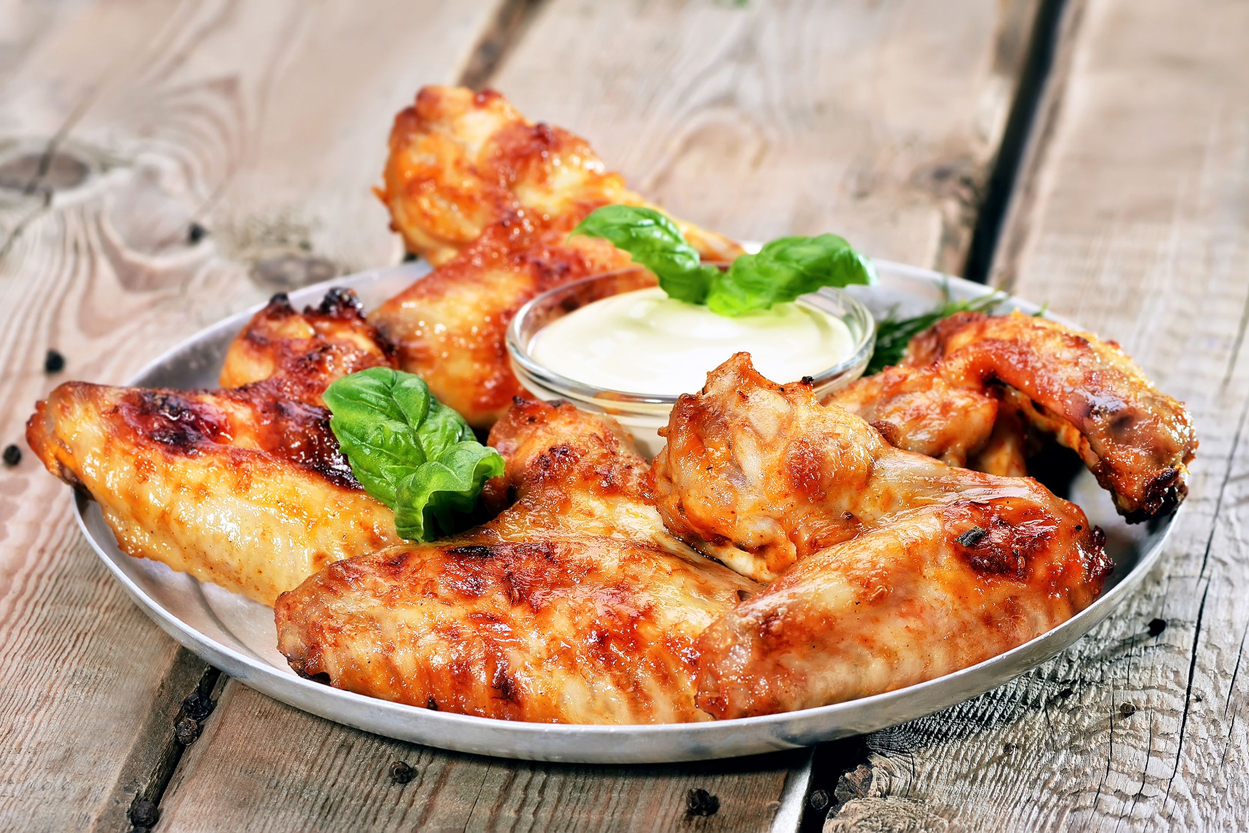 Crispy baked chicken wings on a stainless steel plate with dipping sauce on an outdoor wooden table